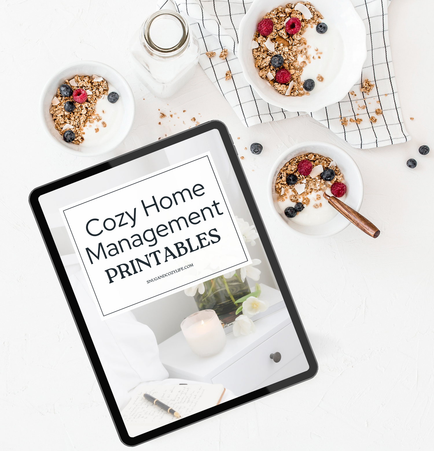 this is a mockup of our cozy home management printables on a tablet screen. This lies on a table with bowls of oats and berries and milke around it.