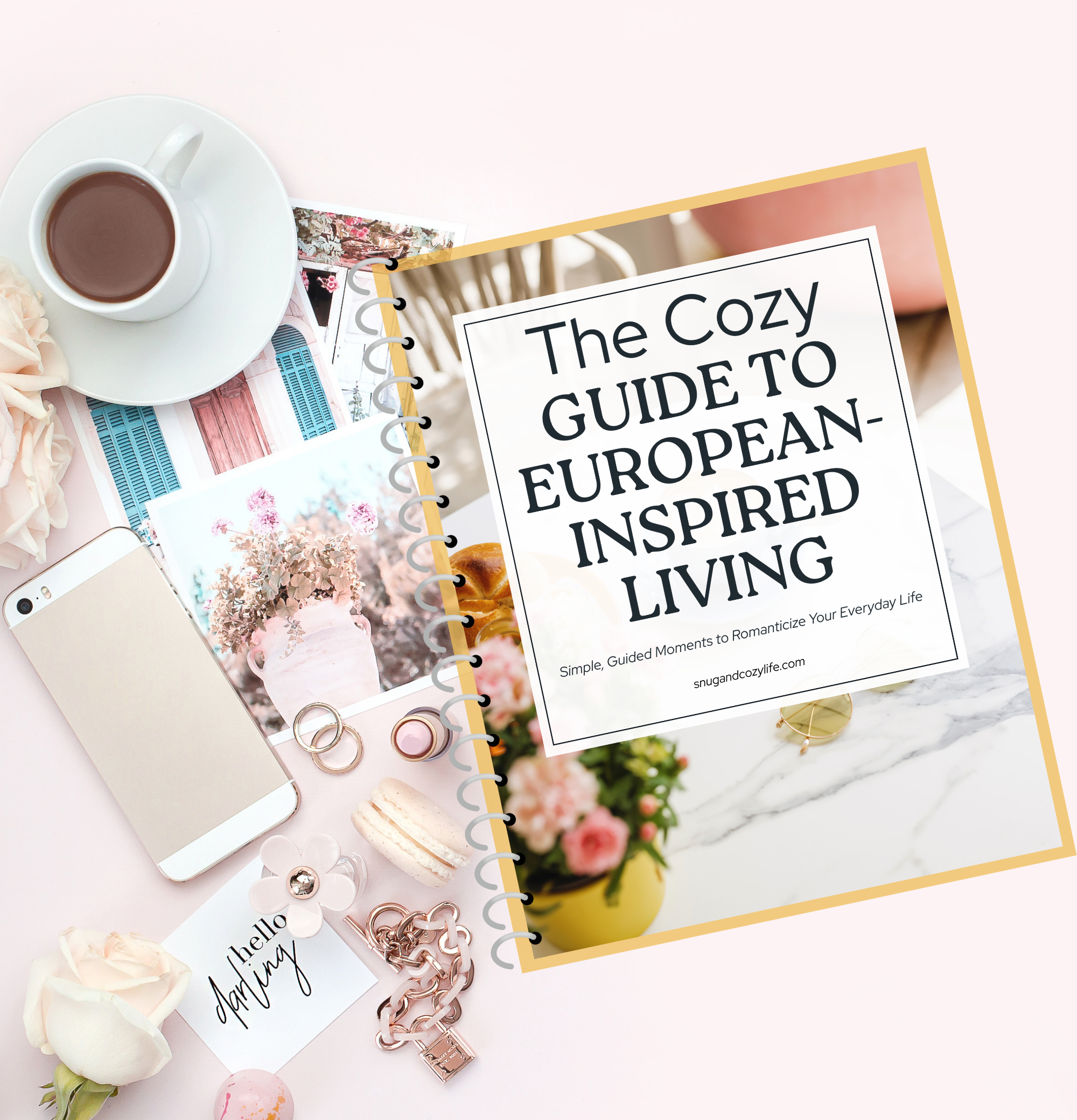 A mockup of the Cozy guide to European-inspired living sitting on a table with a coffee, cellphone, some flowers, notes, and jewelry scattered around it.