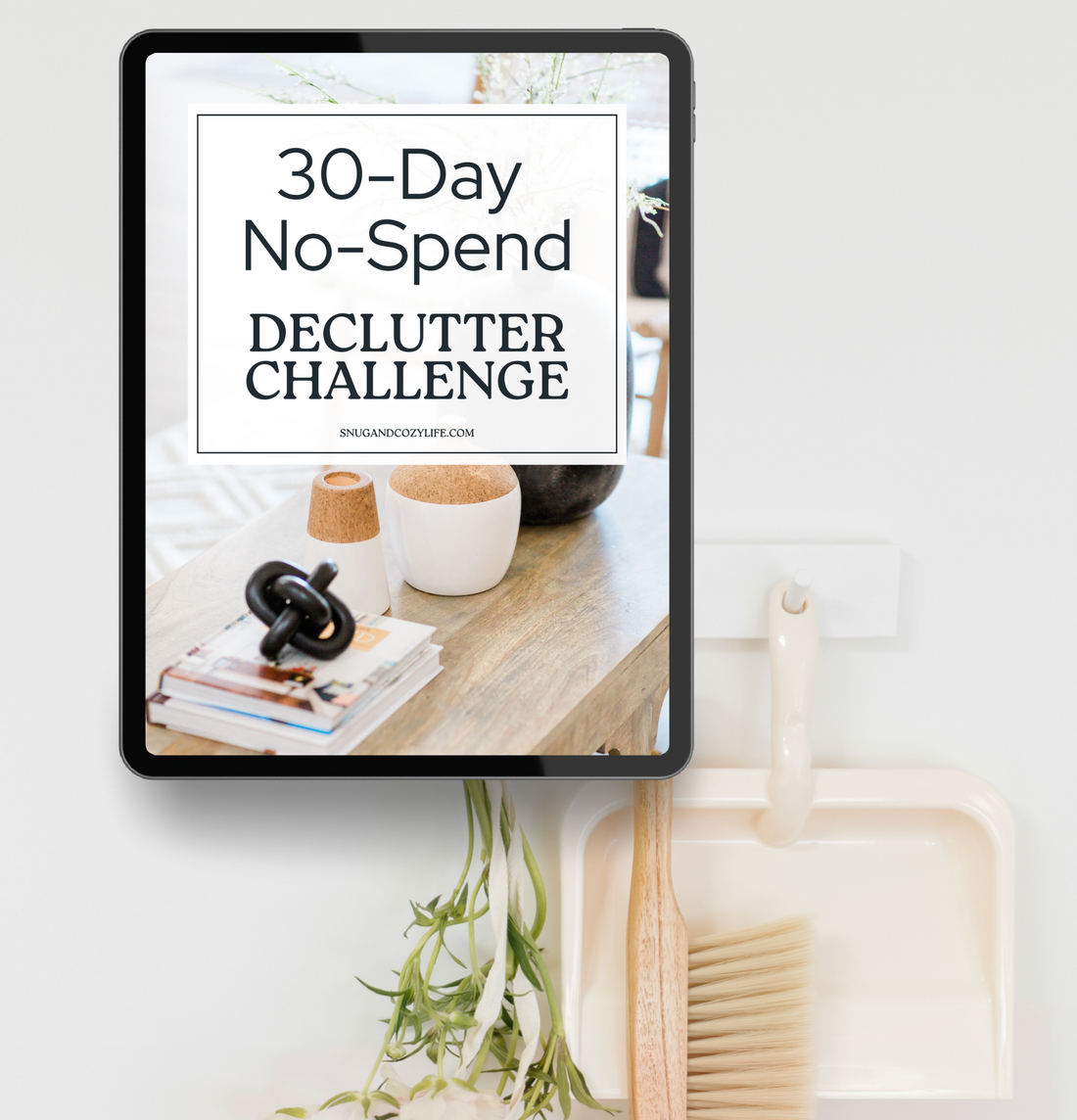 this is a mockup of our 30-Day No-Spend declutter challenge on a tablet screen with a dustpan and brush hanging on a wall behind it.
