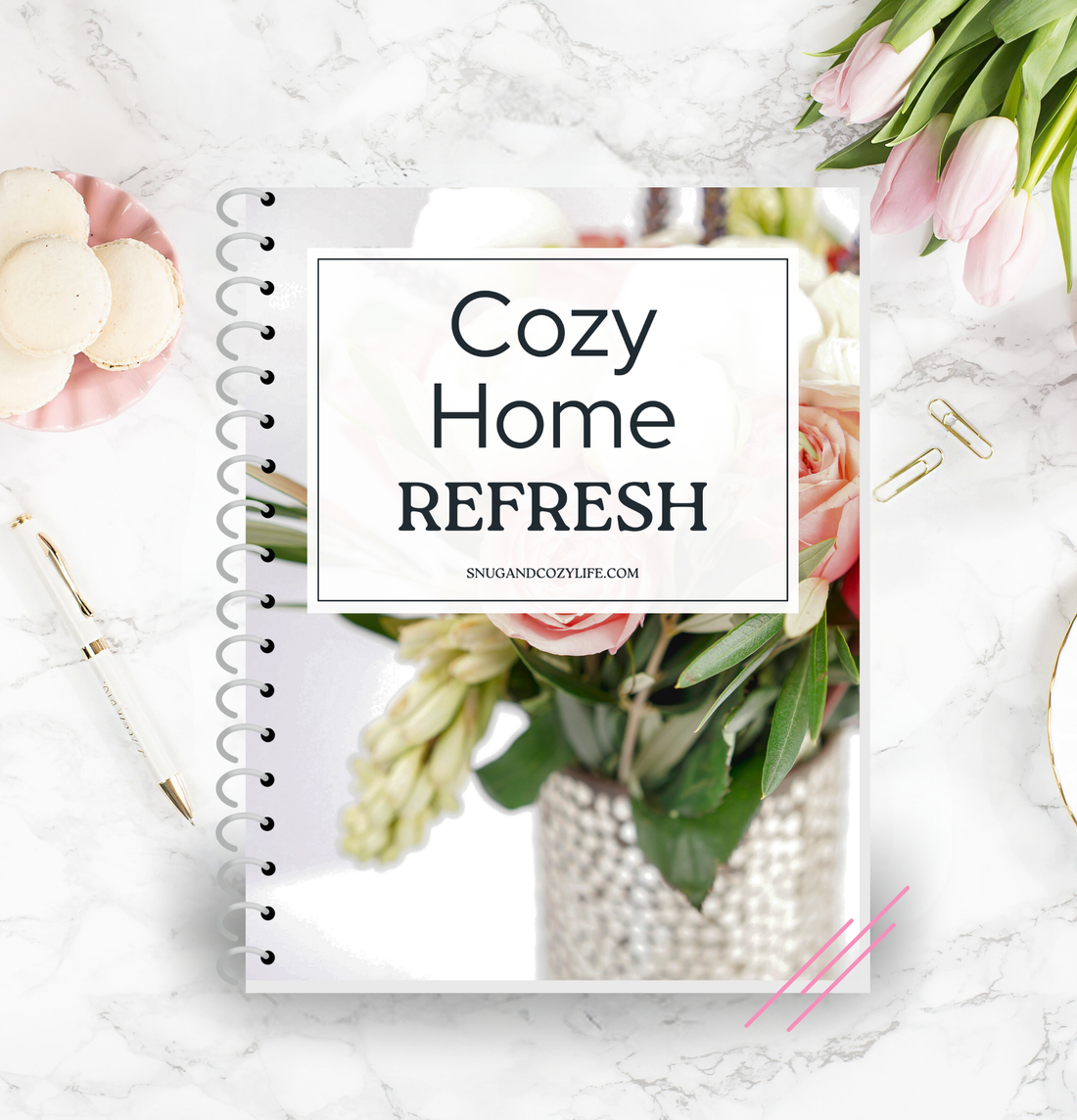 this is a mockup of our cozy home refresh guide and checklist on a binder, which sits on a table top with tulips, macarons, and a pen and paper clips in the background.