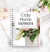 this is a mockup of our cozy home refresh guide and checklist on a binder, which sits on a table top with tulips, macarons, and a pen and paper clips in the background.